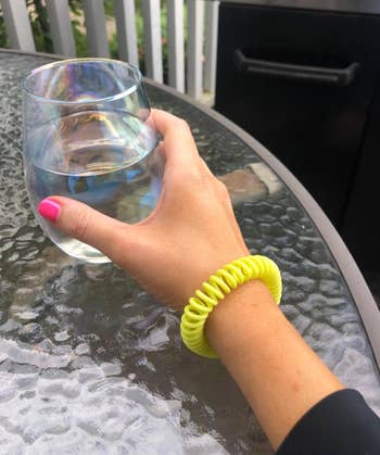Hand with a neon coiled bracelet holds a solid  of h2o  connected  a patio table