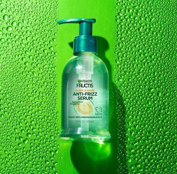 a bluish bottle of anti-frizz serum surrounded by droplets of oil