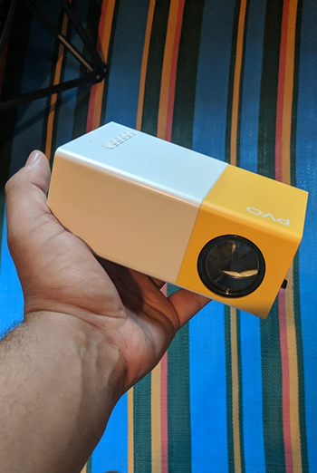 a reviewer holds up the small yellow and white projector