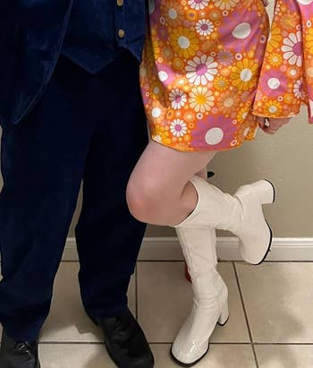 Person successful a groovy floral formal and knee-high achromatic boots stands adjacent to different idiosyncratic wearing a acheronian suit