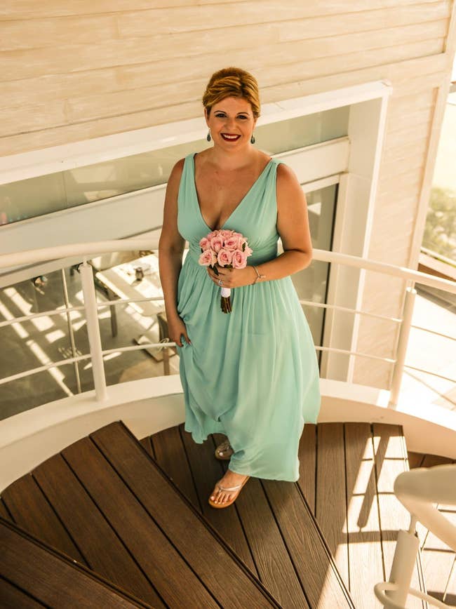 reviewer in a flowy, sleeveless v-neck gown holding a bouquet, standing on a staircase