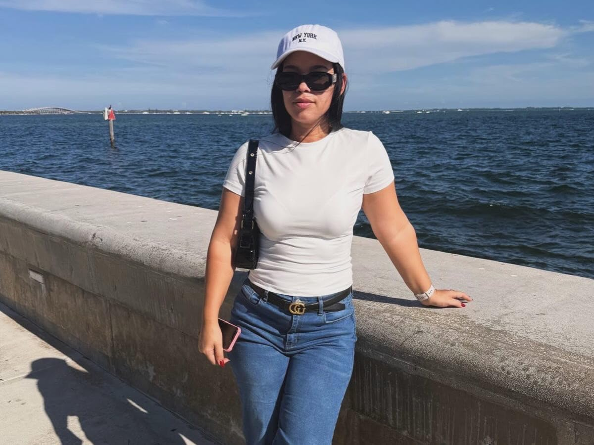 Person wearing a achromatic  headdress  and sunglasses, successful  a casual achromatic  apical  and jeans, stands by a waterfront