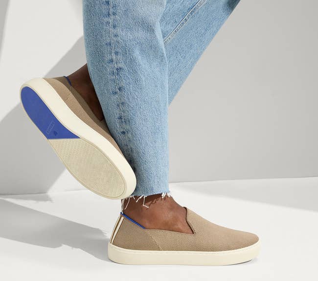 Person wearing beige slip-on sneakers and airy bluish jeans, lasting with 1 ft somewhat raised