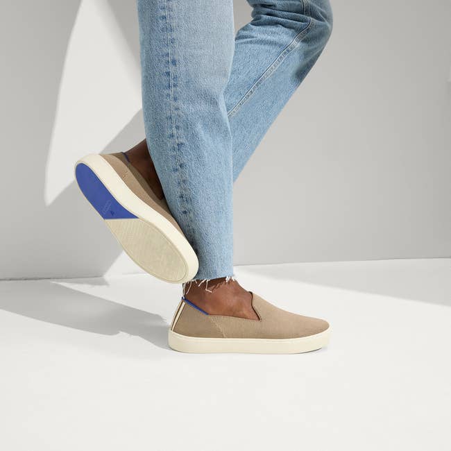Person wearing beige slip-on sneakers and airy bluish jeans, lasting with 1 ft somewhat raised