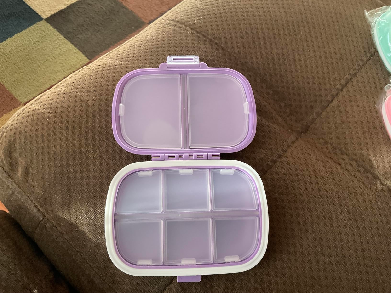 Open multi-compartment lunchbox with a purple lid, connected  a brownish  couch
