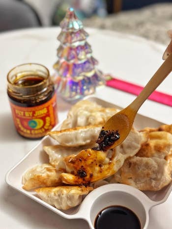 Plate of dumplings with spicy condiment  being added, a jar of 