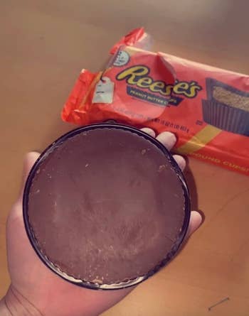 Hand holding a giant Reese's Peanut Butter Cup, with its packaging visible in the background. Perfect for chocolate and peanut butter fans