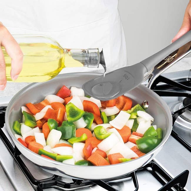Person sautéing vegetables and pouring oil over the veggies with the measuring spatula 