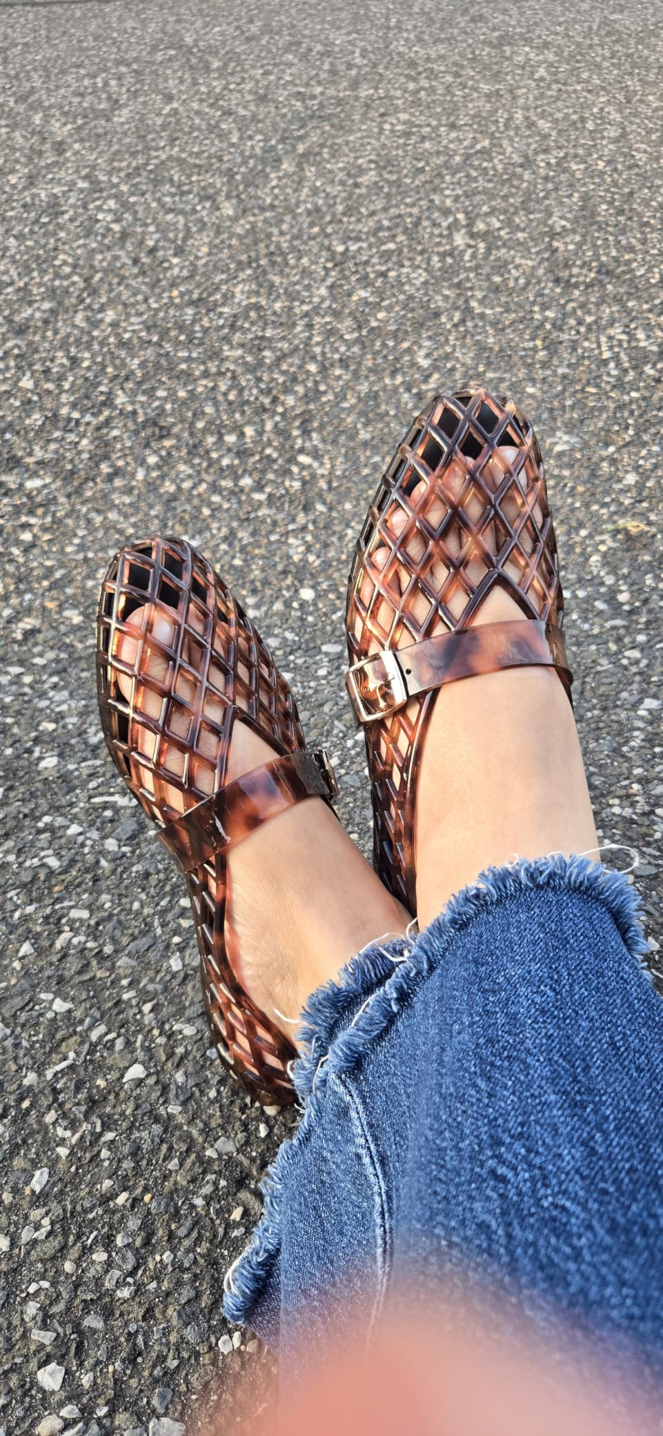 Woven integrative  sandals connected  feet with frayed hem jeans, acceptable   against a textured pavement background