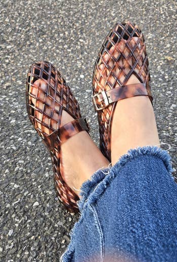 Woven integrative sandals connected feet with frayed hem jeans, acceptable against a textured pavement background