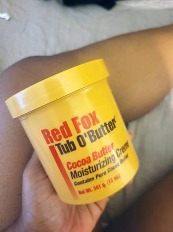 A idiosyncratic   holding a tub of Red Fox Tub O'Butter cocoa food  moisturizing creme