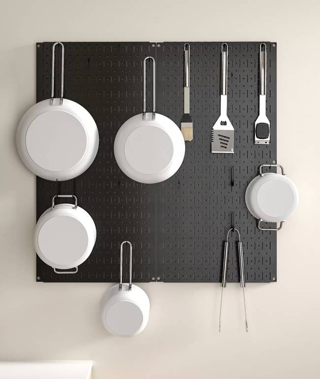 Black pegboard with pots and spatulas hanging from hooks