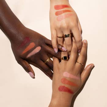 Three hands showcasing different shades of color corrector swatches on their skin
