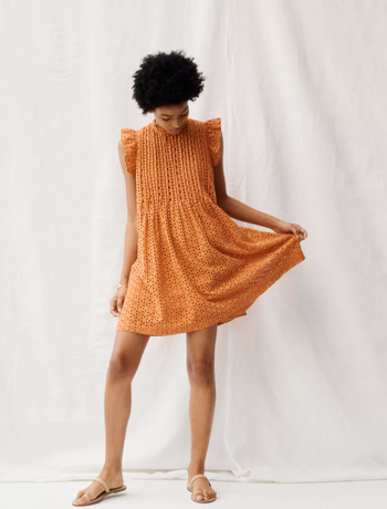 a model in a yellow/orange eyelet dress with ruffled sleeves