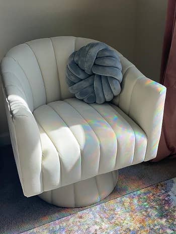 A stylish white modern chair with a gray decorative pillow, bathed in natural sunlight