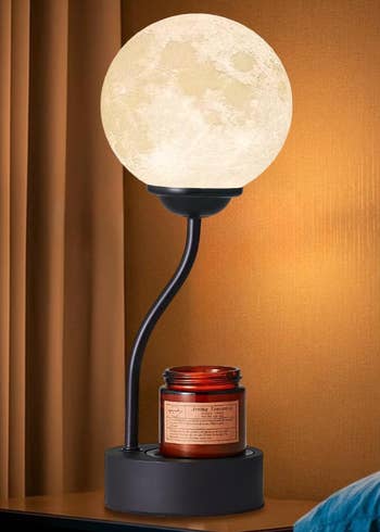 Moon lamp with a curved stand and a red candle on a modern side table, creating a warm and cozy ambiance