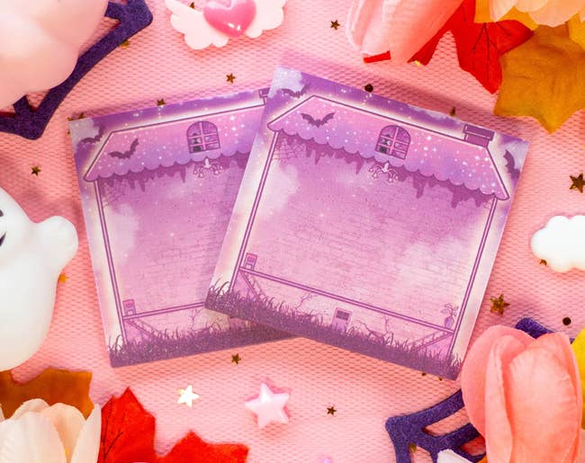 Two decorative, witch-themed notepads with a whimsical location design, surrounded by festive autumn and Halloween decorations
