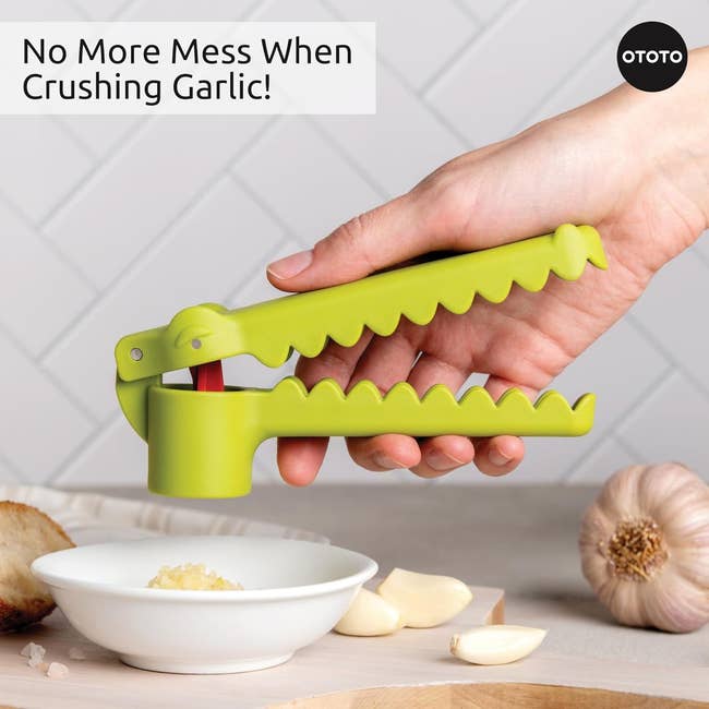 Hand using a crocodile-shaped garlic press over a bowl; text highlights its no-mess feature