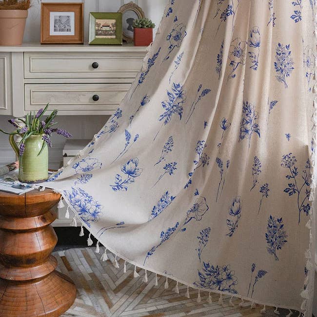 panel curtain with blue floral pattern and tassels on edges hanging up in a living room window 