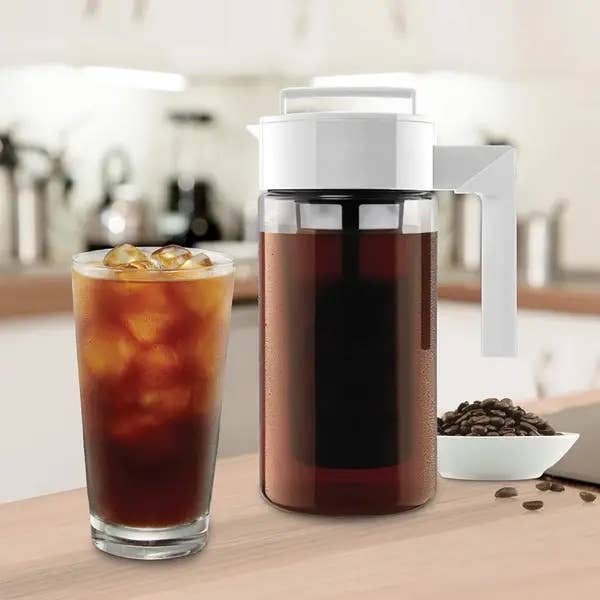 the white cold brew maker next to a glass filled with iced coffee
