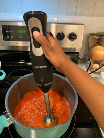 writer holding the immersion blender in a pot of sauce
