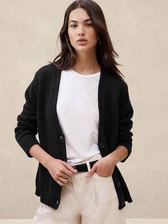 Woman in a casual chic outfit with a black cardigan and white top, posing for a fashion look
