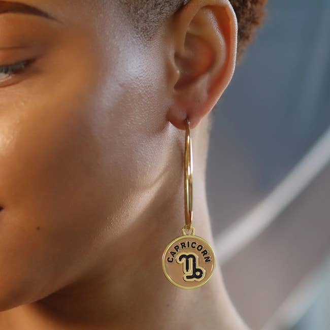 model wearing large gold hoops with capricorn charm