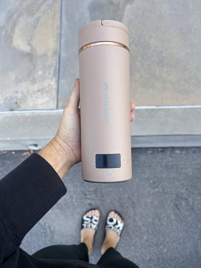 Person holding a portable electrical kettle with a tiny integer show and powerfulness button, wearing achromatic covering and patterned sandals