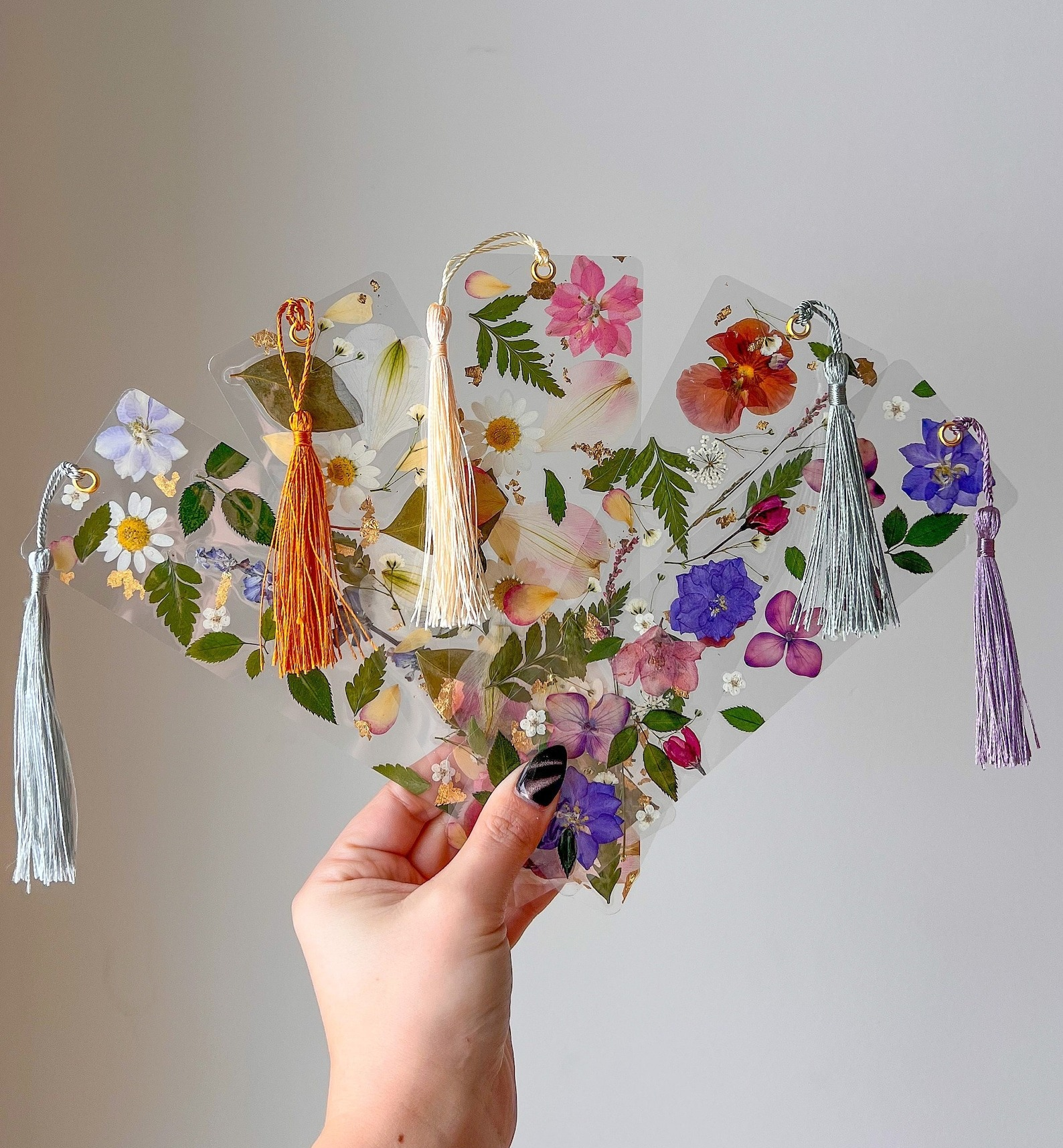 person holding up five clear bookmarks with flowers pressed in them
