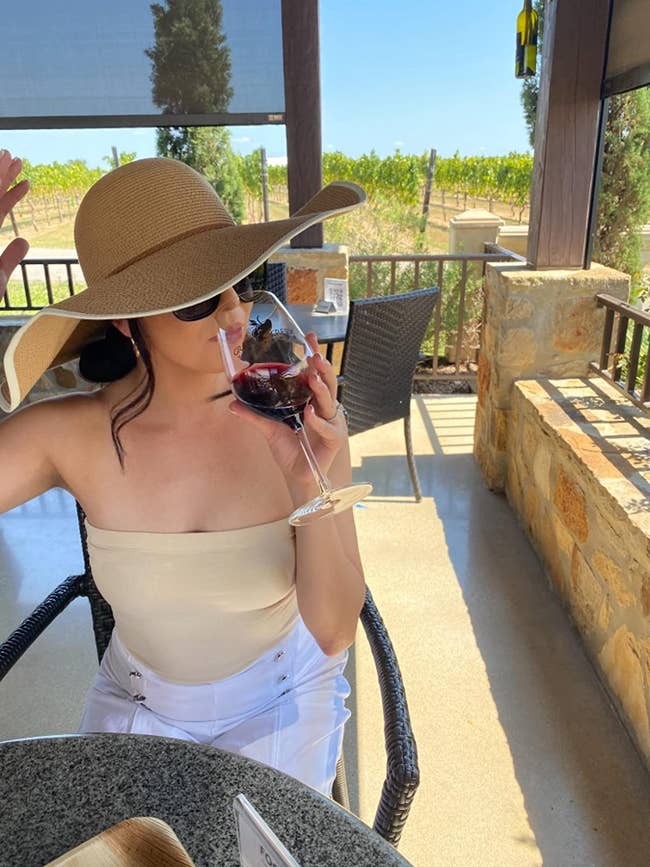 reviewer wearing tan floppy hat, sipping wine