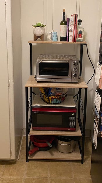 Reviewer image of light wooden and black metal four-tier microwave cart with microwave, toaster oven, and cooking tools on each shelf