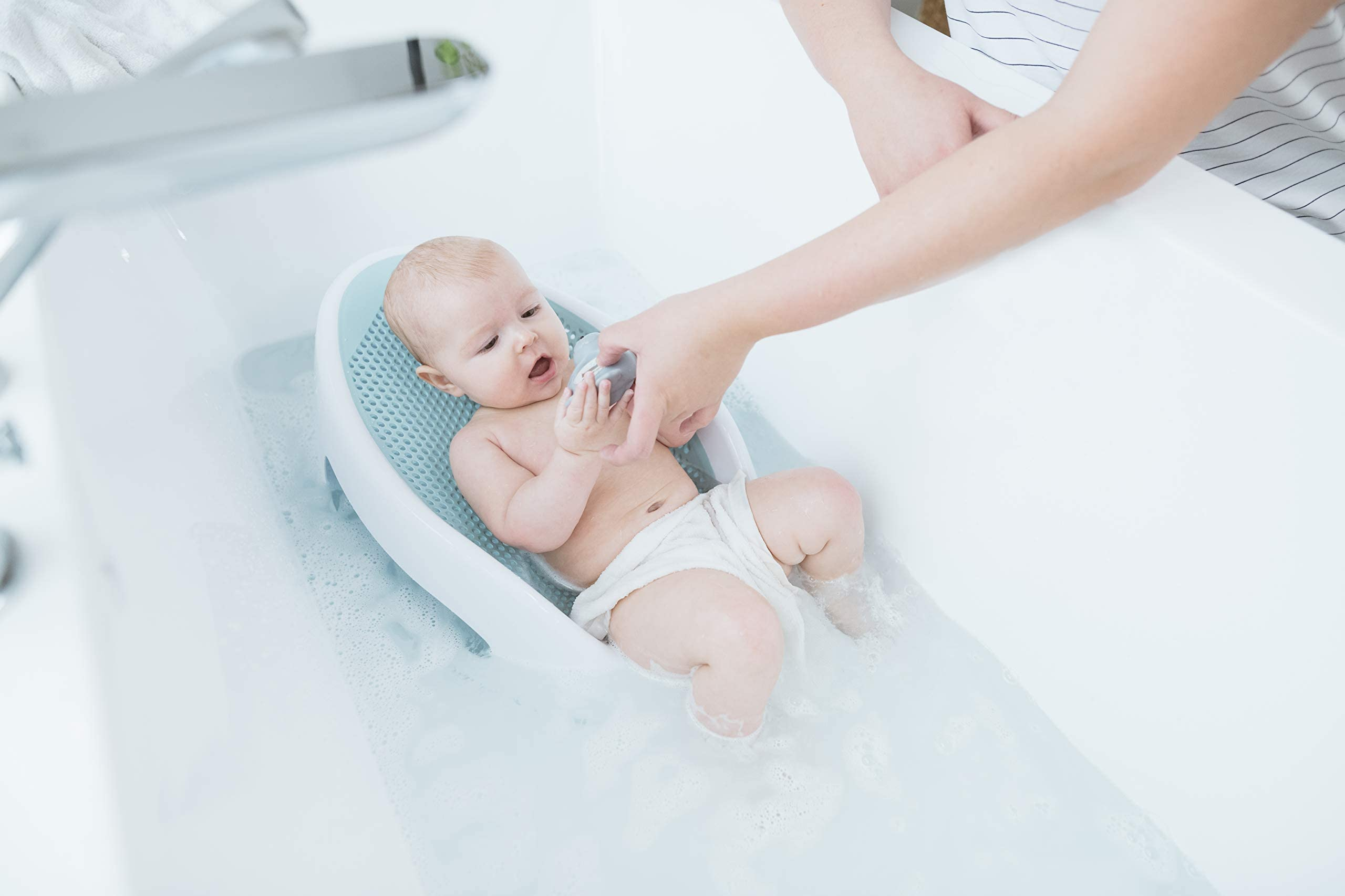 Baby seated successful  a bath spot   successful  a bathtub, engaging with a artifact  portion    an big  manus  offers support