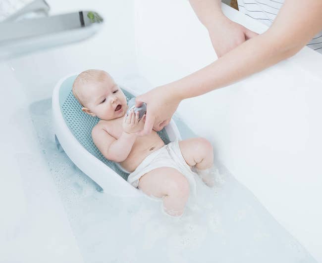 Baby seated successful a bath spot successful a bathtub, engaging with a artifact portion an big manus offers support