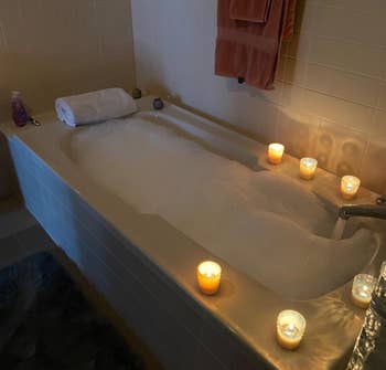 reviewer's tub filled with bubbles and surrounded by candles