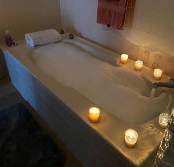 reviewer's tub filled with bubbles and surrounded by candles