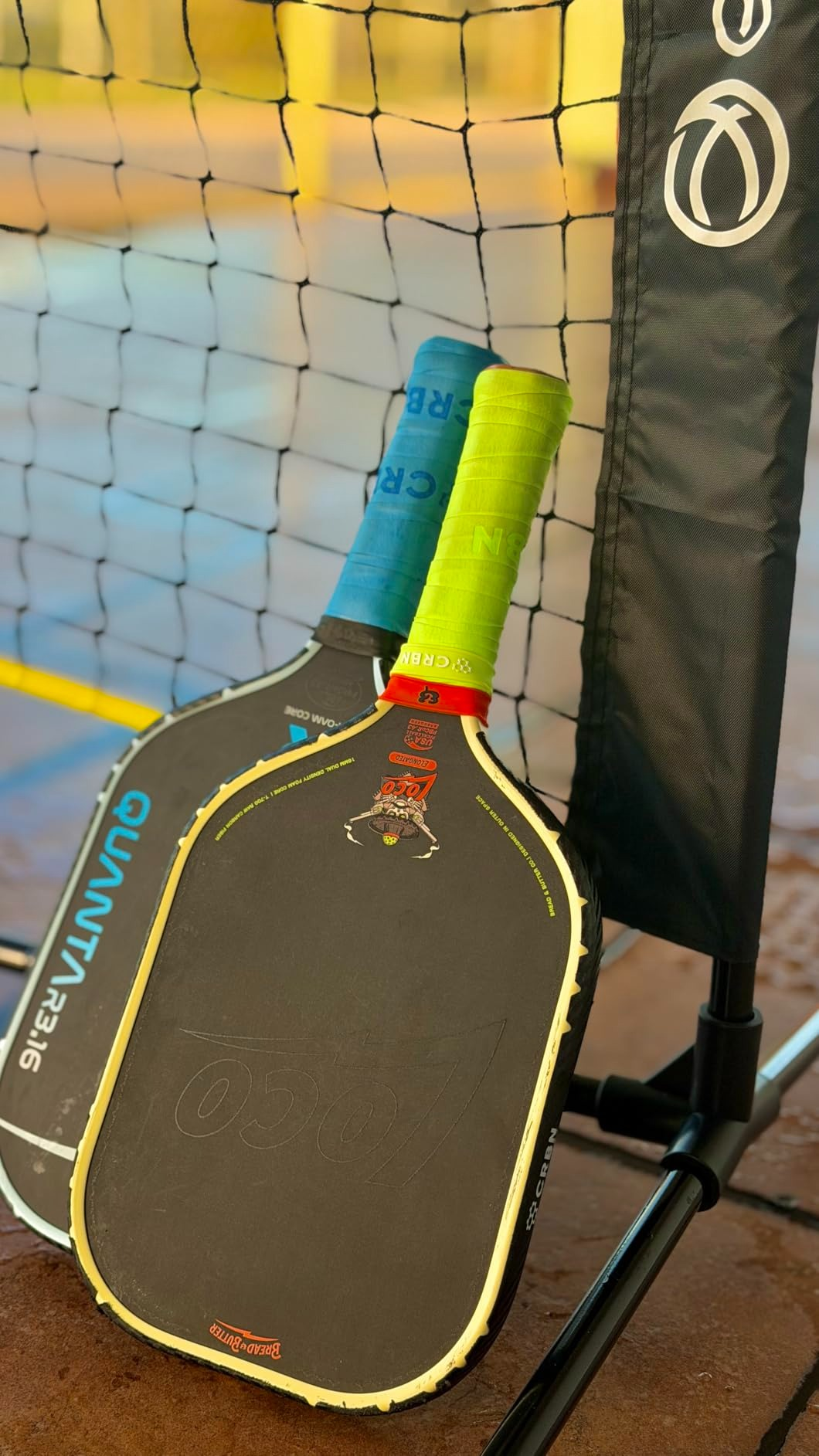 Two pickleball paddles leaning against a nett  connected  a court