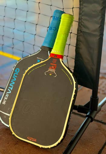 Two pickleball paddles leaning against a nett connected a court