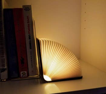 reviewer's Illuminated book-shaped lamp on a shelf beside stacked books