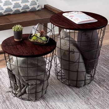 Two nesting end tables in grey holding pillows and blankets