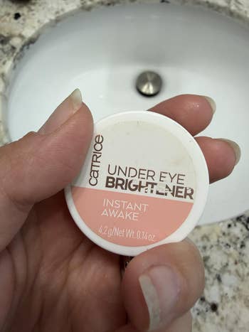 A manus holds a tiny instrumentality of Catrice Under Eye Brightener