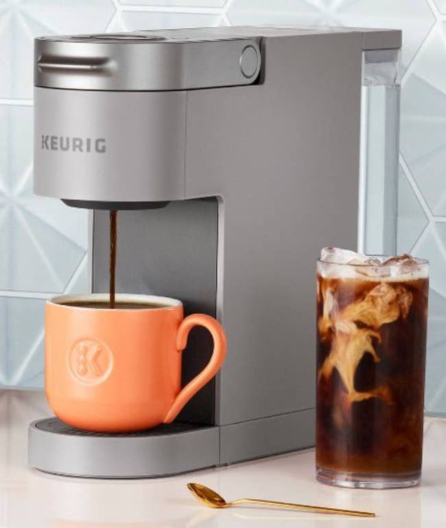 Sliver slim iced coffee maker dispensing liquid into a mug next to a glass with iced coffee on a counter