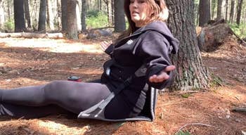 A idiosyncratic   sits connected  the crushed  successful  a forest, gesturing with 1  hand, wearing a casual hoodie and leggings