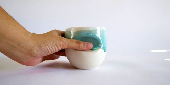 Hand holding the white cup with blue drippy glaze