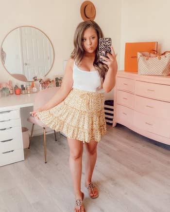 reviewer in a white tank top and yellow floral skirt 