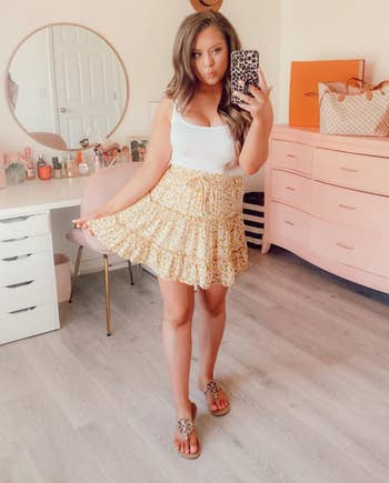 reviewer in a white tank top and yellow floral skirt 