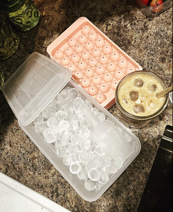 Ice tray full of small sphere shaped ice cubes with a clear bucket 