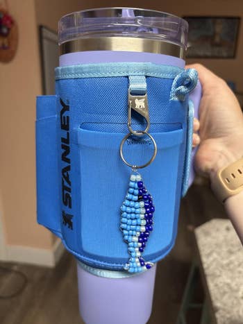 Travel tumbler with bluish  cloth  holder and a decorative bluish  beaded keychain featuring a food  design