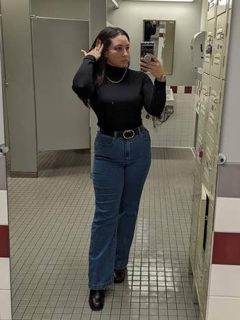 Person wearing a achromatic apical and high-waisted jeans, taking a reflector selfie successful a locker room