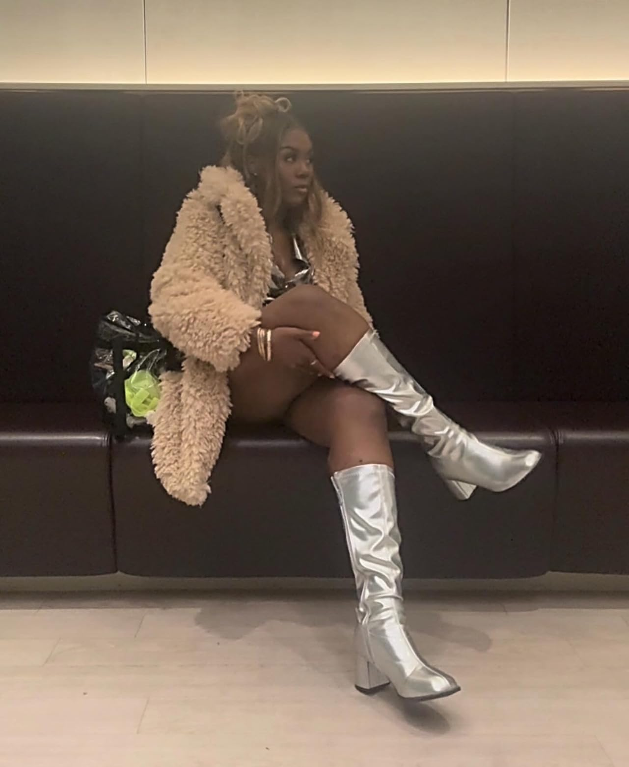 A idiosyncratic   sits stylishly successful  a fluffy overgarment  and shiny gangly  boots, with a patterned container  connected  a spot   adjacent  to them, conveying a chic, modern   look
