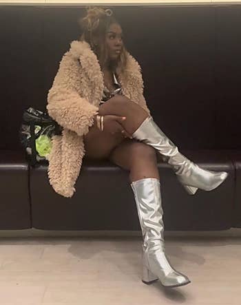 A idiosyncratic sits stylishly successful a fluffy overgarment and shiny gangly boots, with a patterned container connected a spot adjacent to them, conveying a chic, modern look